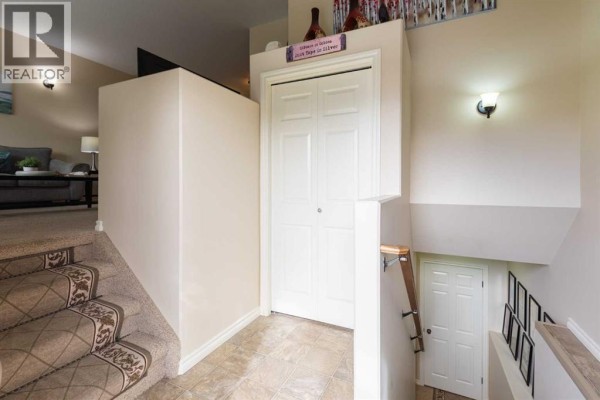 Interior hallway view showing stairs, a bi-fold closet door, and another door at the bottom of the stairs. - 106 Ranchlands Way Ne, Medicine Hat