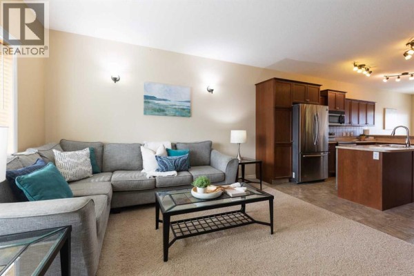 Living room with a gray sectional sofa, coffee table, and open concept view to the kitchen area. - 106 Ranchlands Way Ne, Medicine Hat