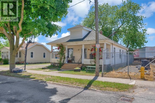 Street view of a cream-colored house with a covered porch, surrounded by trees and fences. - 106 St. George Street, Chatham