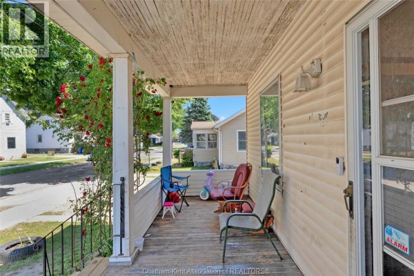 View of the covered wooden porch with chairs and a child's pink ride-on toy. - 106 St. George Street, Chatham