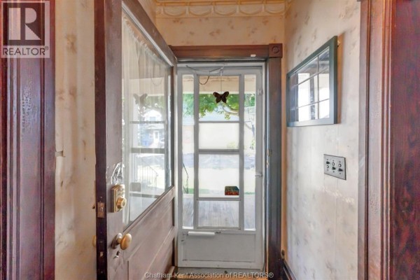 Interior view of the front entryway with a wooden door and a screen door leading outside. - 106 St. George Street, Chatham