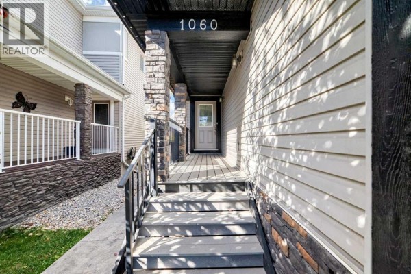 Covered front porch entryway with stone pillars and the house number "1060" above the door. - 1060 Kingston Crescent Se, Airdrie