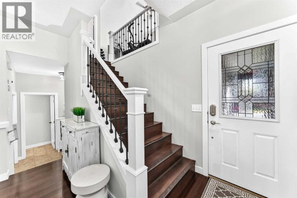 Interior front foyer with a dark wood staircase, white banister, and a decorative white console table. - 1060 Kingston Crescent Se, Airdrie