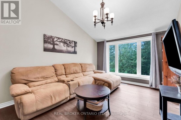 Living room with a large beige sectional sofa, coffee table, and a large window overlooking trees. - 106008 Southgate Rd 10 Line, Southgate