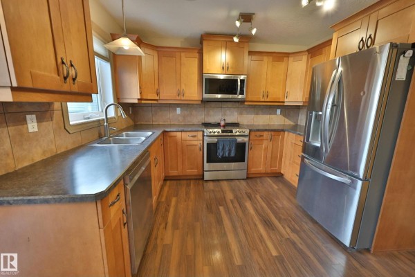 U-shaped kitchen with light wood cabinets, stainless steel appliances, and laminate flooring. - 10603 95 St, Morinville
