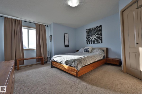 Bedroom with a queen-size bed, light blue walls, tan curtains, and carpeted floor. - 10603 95 St, Morinville