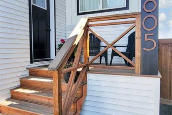 Wooden steps and railing lead to the front door of a white house with a black door. - 10605 114a Street, Grande Prairie