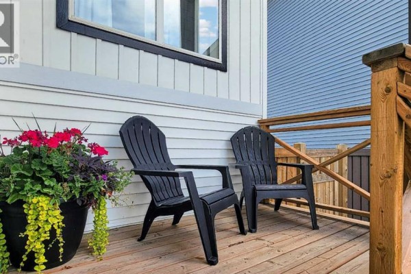 Two dark gray Adirondack chairs sit on a wooden deck next to a potted plant. - 10605 114a Street, Grande Prairie