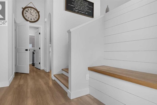 Hallway interior with light wood flooring, white shiplap walls, a wooden bench, and an arched doorway. - 10605 114a Street, Grande Prairie