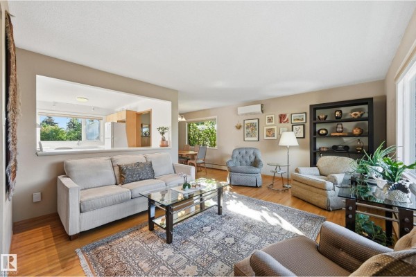 Living room with beige walls, hardwood floors, two sofas, two armchairs, a glass coffee table, and a patterned rug. - 10607 74 St Nw, Edmonton