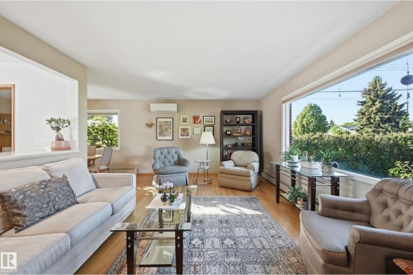 Living room with large picture window overlooking trees, hardwood floors, seating area, and artwork on the walls. - 10607 74 St Nw, Edmonton