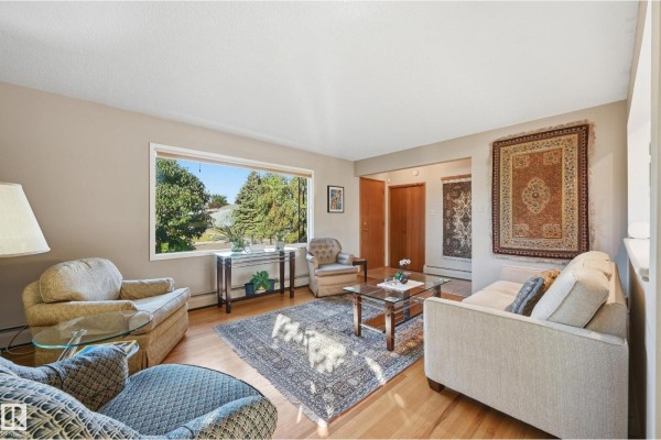 Living room with a large window offering a view of trees, hardwood floors, and various seating options. - 10607 74 St Nw, Edmonton