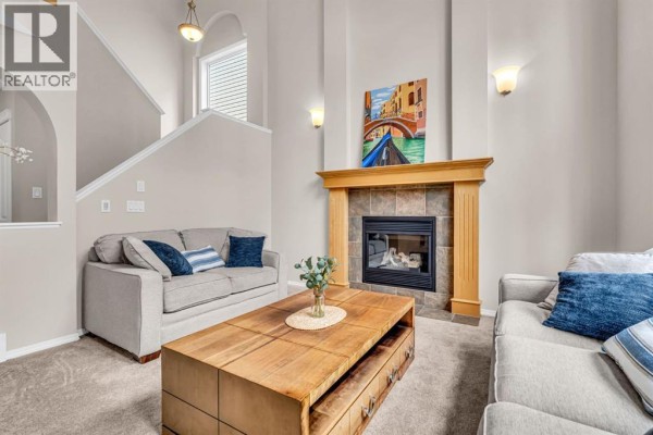 Living room with a fireplace, a staircase, neutral furniture, and a large wooden coffee table. - 1062 Tuscany Drive Nw, Calgary