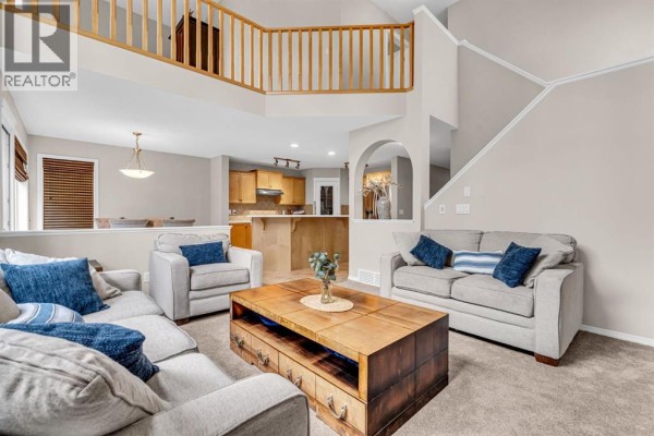 Living room with a mezzanine, view of the kitchen and dining area, and multiple seating areas. - 1062 Tuscany Drive Nw, Calgary