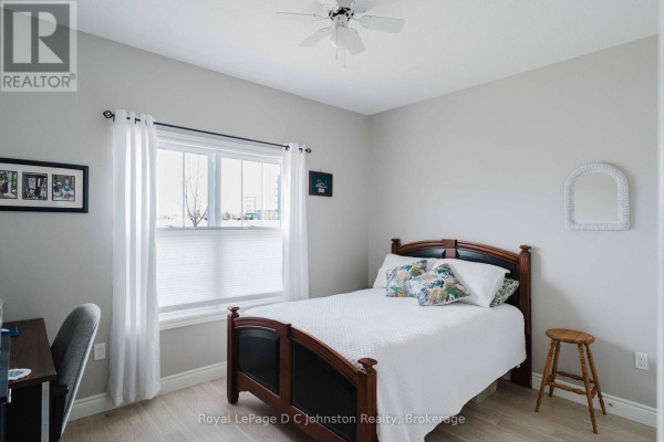 Bedroom with a wooden bed frame, white bedding, a desk, and a window with blinds. - 1062 Waterloo Street, Saugeen Shores