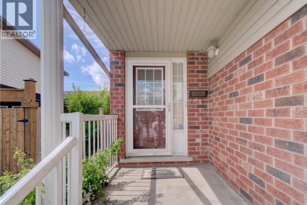 Covered front porch with brick pillars, white railing, and a red brick facade. - 1064 Copper Leaf Crescent, Kitchener