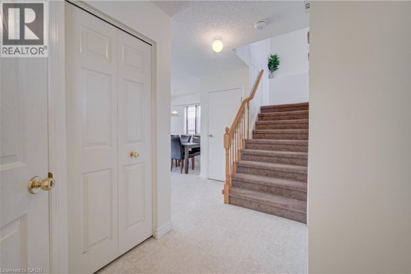 Hallway view with a closet, carpeted stairs with wooden railings, and a dining area in the distance. - 1064 Copper Leaf Crescent, Kitchener