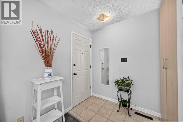 Interior foyer with tiled floor, light grey walls, a white door, and a tall storage cabinet. - 10647 Shillington Crescent Sw, Calgary