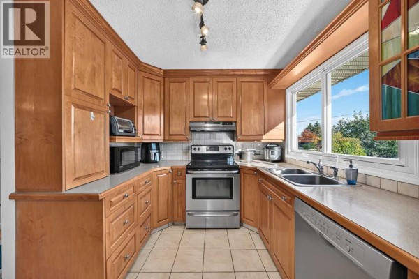 U-shaped kitchen with light wood cabinets, stainless steel appliances, and a large window. - 10647 Shillington Crescent Sw, Calgary