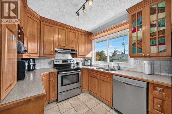 Another view of the U-shaped kitchen showing the sink, dishwasher, and window with stained glass detail. - 10647 Shillington Crescent Sw, Calgary