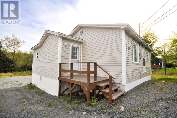 Rear of the beige house, showing a wooden deck with stairs, windows, and vinyl siding. - 1067 Main Road, Dunville