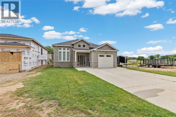 Side exterior view of a modern brick and stone house with a driveway and green lawn. - 1067 Maple, Kingsville