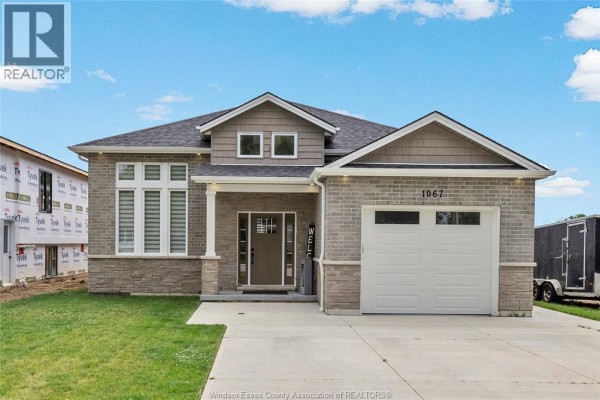 Front exterior of a modern brick and stone house with a driveway and green lawn. - 1067 Maple, Kingsville
