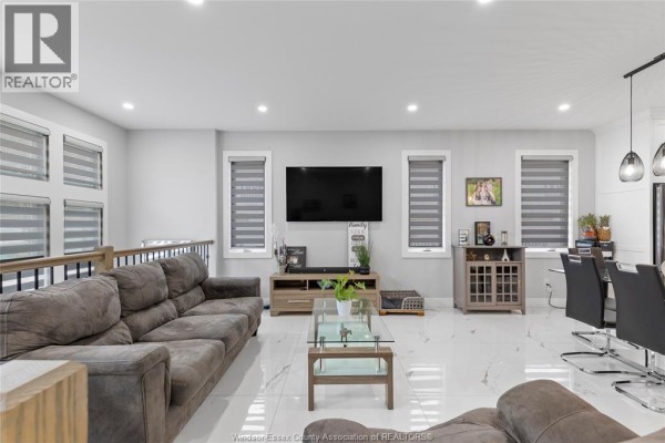 Living room with a large sectional sofa, television, glass coffee table, and dining area. - 1067 Maple, Kingsville