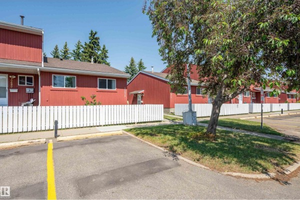 View of red townhouses with white picket fences and trees along the street. - 10678 Beaumaris Rd Nw, Edmonton