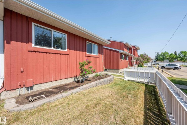 Close-up of red townhouse exterior showing wooden siding, window, and small garden bed. - 10678 Beaumaris Rd Nw, Edmonton
