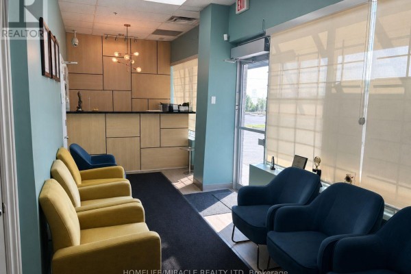 Waiting area with blue and yellow chairs, reception desk, and light wood paneling. - 107 - 1339 Khalsa Drive, Mississauga