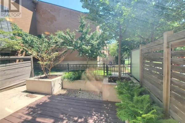 Outdoor patio with wooden decking, planters containing plants and trees, and a wooden privacy fence. - 107 - 383 Prince Of Wales Drive, Mississauga