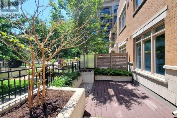 Townhouse exterior with brick walls and large windows overlooks a patio with wood decking and greenery. - 107 - 383 Prince Of Wales Drive, Mississauga