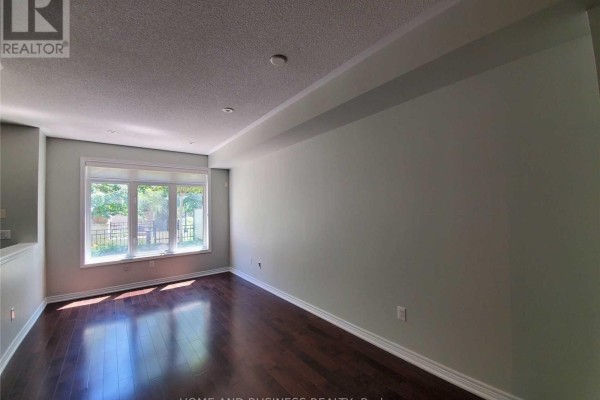 Empty living room with dark hardwood floors, light green walls, and a large window with a view of trees. - 107 - 383 Prince Of Wales Drive, Mississauga