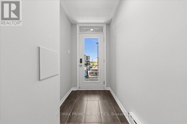 Interior view of a hallway with light grey walls and dark tiled floor, leading to a glass door. - 107 - 657 Makwa Private, Ottawa