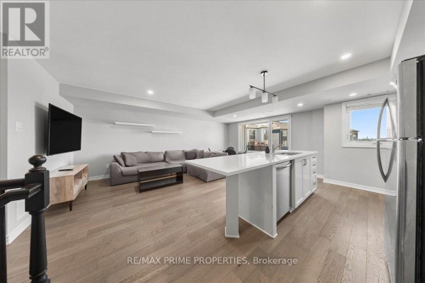Open concept living and kitchen area with a large sectional sofa, island, and stainless steel appliances. - 107 - 657 Makwa Private, Ottawa