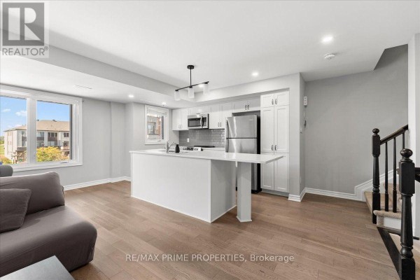 Kitchen area with white cabinets, quartz island, stainless steel appliances, and a window overlooking the exterior. - 107 - 657 Makwa Private, Ottawa