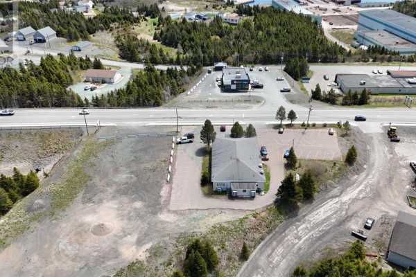 Side view of the commercial building showing light siding, small windows, ventilation pipes, and a trash bin. - 107-115 Mcgettigan Boulevard, Marystown