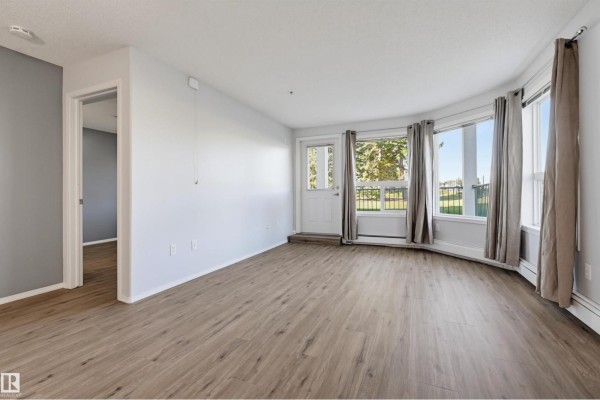 View of the living area, kitchen, and a hallway, with a door to the balcony. - #107 13635 34 St Nw, Edmonton