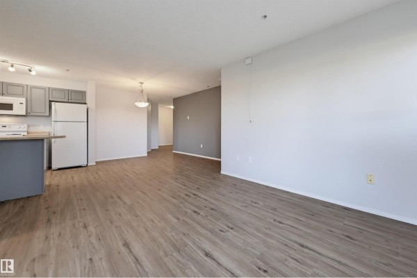 Kitchen and living area with light grey walls, light brown flooring, and grey cabinets. - #107 13635 34 St Nw, Edmonton