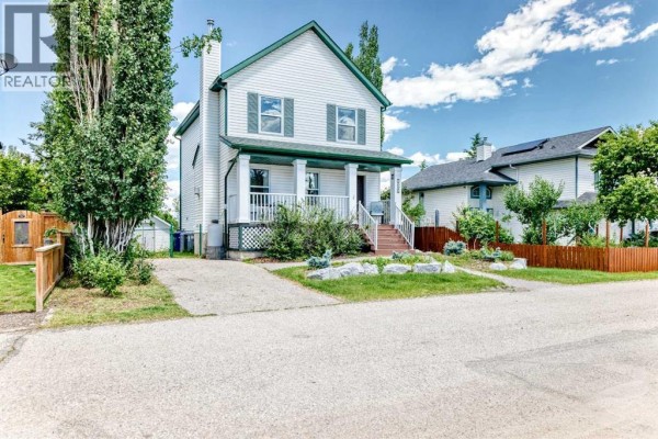 View of a grassy backyard surrounded by mature trees. - 107 2a Avenue Nw, Diamond Valley