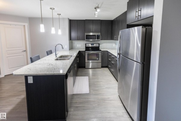 U-shaped kitchen with dark grey cabinets, granite countertops, and stainless steel appliances. - #107 3670 139 Av Nw, Edmonton