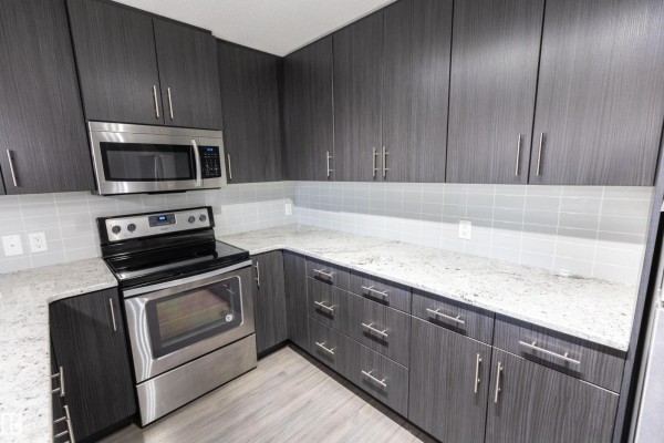 Kitchen with grey cabinetry, white tiled backsplash, granite countertops, and stainless steel stove. - #107 3670 139 Av Nw, Edmonton