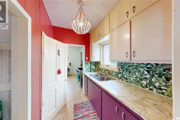 Narrow kitchen with red walls, patterned backsplash, and a chandelier above the sink. - 107 3rd Avenue E, Scott