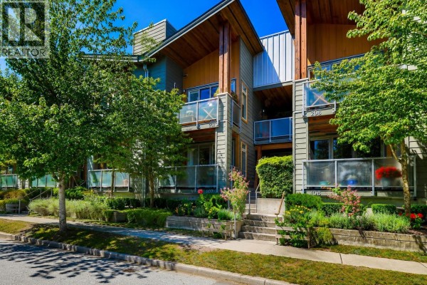 Front view of a three-story apartment building with balconies and trees. - 107 40147 Government Road, Squamish