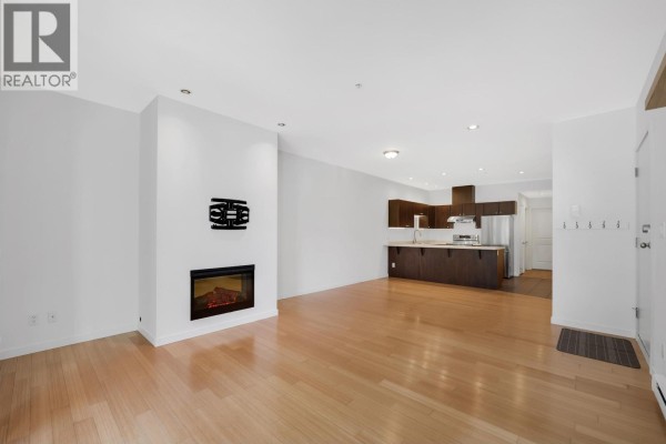 Living area with a fireplace, light wood floors, and an open kitchen. - 107 40147 Government Road, Squamish