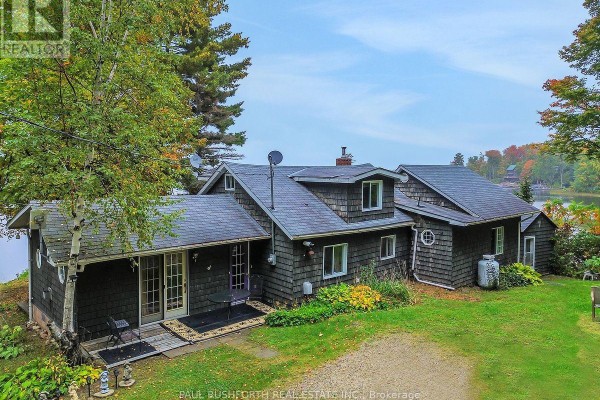 View of the dark grey cedar shingled house with a propane tank and a circular window on the side. - 107 Beck Shore Road, Drummond/north Elmsley
