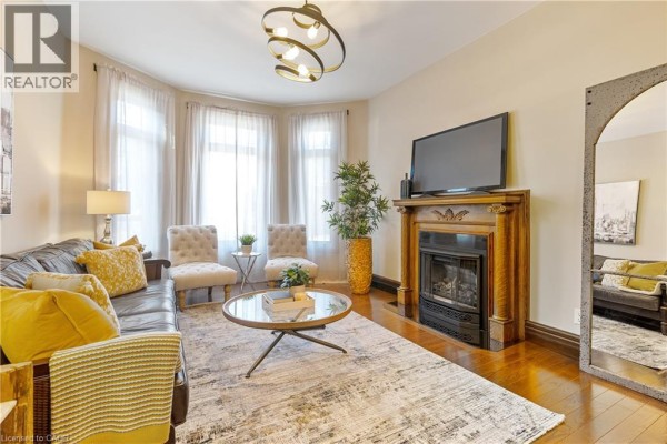 Living room with a fireplace, leather sofa, upholstered chairs, and bay windows. - 107 Catharine Street S Unit# Main Flr, Hamilton