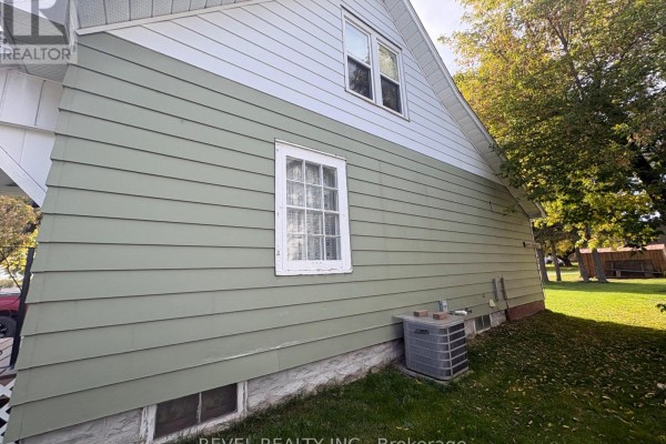Side exterior view of the house showing green siding, a white upper level, and a small basement window. - 107 Fifteenth Avenue, Cochrane