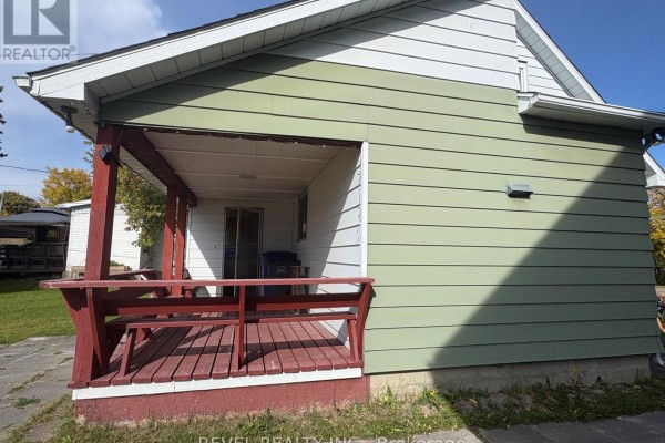Side exterior view of the house with a red wooden deck and porch attached to the white siding. - 107 Fifteenth Avenue, Cochrane